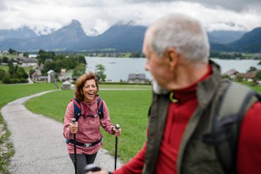 Dağlarda birlikte yürüyüş yapan aktif yaşlı bir çiftin portresi. Kıdemli turistler istikrar için yürüyüş direğiyle yürüyorlar.
