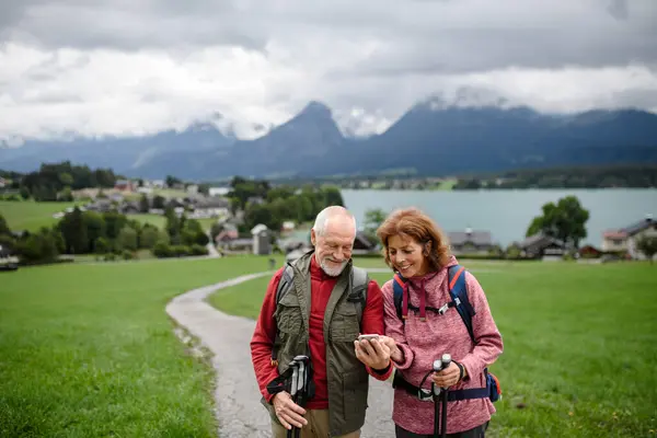 Active elderly couple hiking together in mountains, enjoying nature. Senior tourists looking at route on a smartphone, in online map.