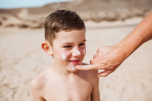 Boy with sunscreen lotion on face. Young boy si protected from sun with sunscreen. Concept of family beach summer vacation with kids.