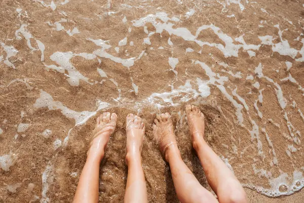 Close up of feet on beach with sea water beneath. Sea foam and warm water soaking legs.
