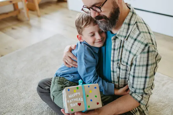 Dad get handmade gift from little son, present wrapped in diy homemade wrapping paper. Father embracing boy. Happy Fathers day concept.