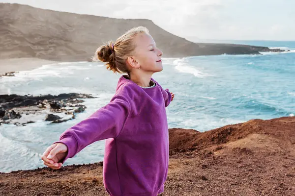 年轻姑娘紧闭双眼 命令海风迎面吹来 美丽的金发姑娘欣赏加那利群岛的自然美景 与孩子共度暑假的概念 图库图片