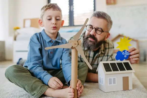 父亲解释可再生能源 教授他年幼的儿子可持续的生活方式 玩太阳能电池板的房子模型 在家里玩风笛 通过游戏学习 图库照片