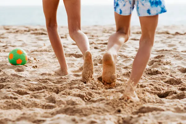 Siblings playing on beach with ball, playing football. Concept of family beach summer vacation with kids. Close up on legs.