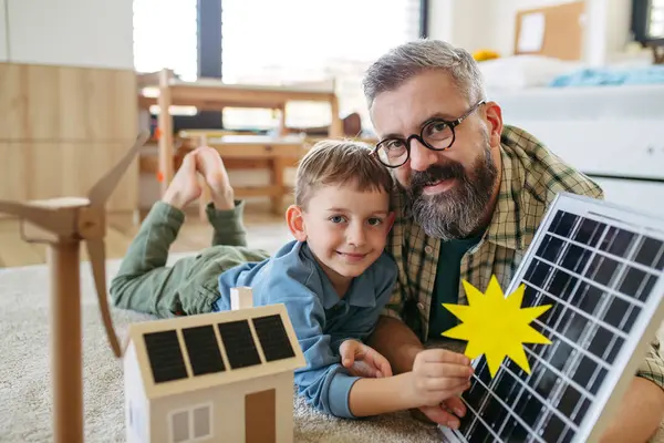 父は再生可能エネルギー 太陽光発電について説明し 息子の持続可能なライフスタイルについて教えています ソーラーパネル付きの家のモデルで遊ぶ 遊びを通して学ぶ ロイヤリティフリーのストック画像