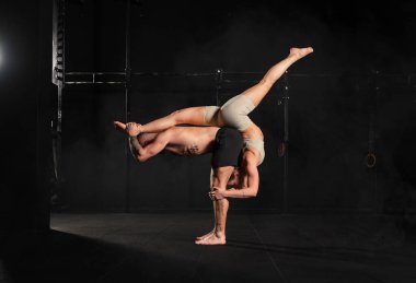 Genç bir erkek ve kadın için akroyoganın ortak spor aktivitesi. Çift spor salonunda birlikte egzersiz yapıyor, karmaşık manevralar yapıyor..