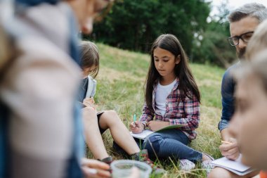 Genç öğrenciler doğayı, biyoloji dersi sırasında orman ekosistemini öğreniyorlar, notlar yazıyorlar. Açık hava eğitimi sırasında bir erkek öğretmen.