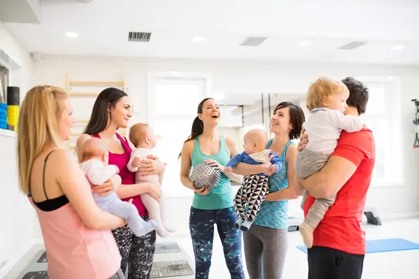 集体健身课 妈妈在健身房和一个婴儿一起锻炼 妈妈们和孩子们在一起的时候很活跃 新的父母朋友 图库照片