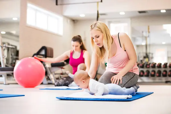 婴儿运动课 父母帮助婴儿提高运动技能 适当地运动在适配球上 儿科理疗师领导集体健身班 有孩子的母亲运动 免版税图库图片