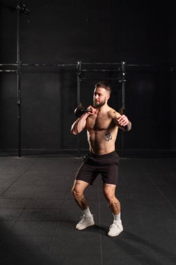 Adam ağırlığını eliyle kaldırıyor, tek kolu dambılı tutuyor, sadece şort giyiyor, göğsü çıplak. Fiziksel ve zihinsel sağlık için rutin çalışma.