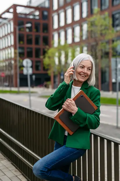 成熟的女商人打电话给智能手机 在城里参加商务会议 美丽的老妇人 白发苍苍地站在城市街道上 在公共汽车上等着 免版税图库照片