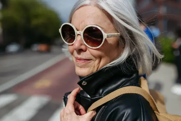 城市街道上长着灰白头发的时尚成熟女人的画像 戴太阳镜等公共交通工具的老年妇女 城市通勤者 免版税图库照片