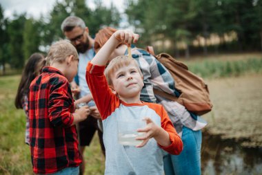 Genç öğrenciler su kalitesini analiz ediyor, biyoloji dersi sırasında gösterge şeritleri ile ph seviyesinde. Ekosistem ve doğa hakkında açık havada aktif eğitim gören kadın öğretmen.