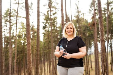Doğada koşmaya hazırlanan kilolu bir kadın. Obezitesi olanlar için açık havada egzersiz yapmak..