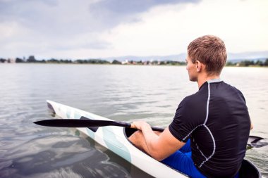 Canoeist man sitting in canoe holding paddle, in water. Concept of canoeing as dynamic and adventurous sport. Rear view, sportman looking at water surface, paddling. clipart