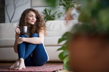 Sabah rutini kıvırcık saçlı, oturma odasında yerde oturan, kahve içen, pencereden dışarı bakan güzel bir kadın için..