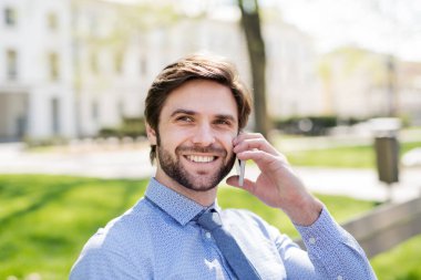 Akıllı telefondan arayan yakışıklı bir iş adamı, şehirde bankta oturuyor. Uzaktan çalışıyor, iş toplantısını bekliyor. Müdür gülümsüyor, şehir ortamında açık havada..