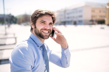 Şehir sokağında duran akıllı telefondan yakışıklı bir iş adamı arıyor. Uzaktan çalışıyor, iş toplantısını bekliyor. Müdür gülümsüyor, şehir ortamında açık havada..
