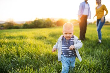 İlkbahar yürüyüşü sırasında ebeveynlerin önünde koşan sevimli bir çocuk. Yeni ebeveynler için mutlu aile anları.