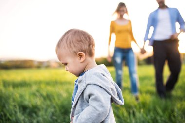 İlkbahar yürüyüşü sırasında ebeveynlerin önünde koşan sevimli bir çocuk. Yeni ebeveynler için mutlu aile anları.