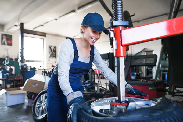 Otomobil servisinde kadın oto tamircisi lastikleri çıkarmak için makineler kullanarak kravat değiştiriyor. Lastikler takılıyor. Kadın otomotiv teknisyeni.