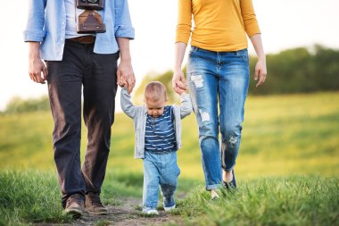 Yeni anne-baba kucağında küçük bir bebekle onu sallıyor. Aile ilkbaharda doğa yürüyüşünde. Mutlu aile anları.