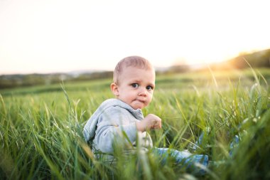 Çimenlerde oturan tatlı bebek. Bahar doğasında ailece yürüyüşe çıkmış bir bebek. Yeni ebeveynler için mutlu aile anları. Portre.
