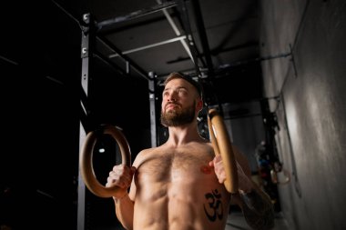 Spor salonunda halkaların yanında duran güçlü adam egzersiz için hazırlanıyor. Güç ve akıl sağlığı için günlük rutin çalışma.