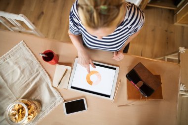 Merkez büroda çalışan yaşlı bir kadın, dizüstü bilgisayarda yazıyor, tabletteki istatistiklere bakıyor. Emekliler emeklilik süresince ekstra para kazanıyor..