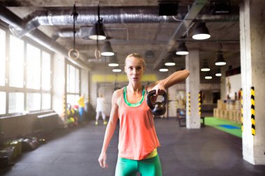 Bir elinde kettlebell tutarak kettlebell ütüsü yapan güzel bir spor kadını. Kadınlar için rutin çalışma fiziksel ve zihinsel sağlık