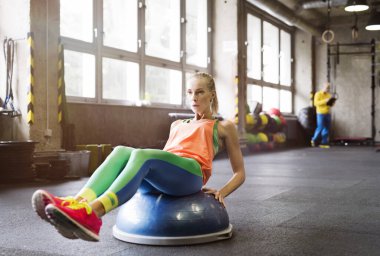 Spor salonunda denge topu üzerinde egzersiz yapan güzel bir kadın. Kadınlar için rutin çalışma fiziksel ve zihinsel sağlık