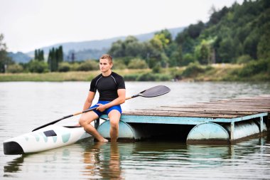 Young canoeist sitting on wooden dock. Concept of canoeing as dynamic and adventurous sport clipart