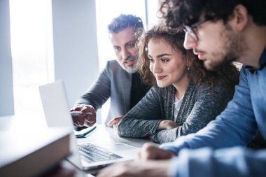 Bir grup iş arkadaşı, dizüstü bilgisayara bakan iş adamları, birlikte bir proje üzerinde çalışıyorlar. Modern ofis alanında beyin fırtınası.