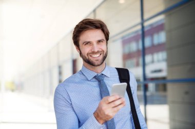 Yakışıklı iş adamı akıllı telefondan kayıyor. Şehir caddesinde yürürken, ofise giderken. Müdür gülümsüyor, şehir ortamında açık havada..