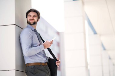 Yakışıklı iş adamı akıllı telefondan kayıyor. Ofis binasının önünde duruyor ve işe gidiyor. Müdür gülümsüyor, şehir ortamında açık havada..