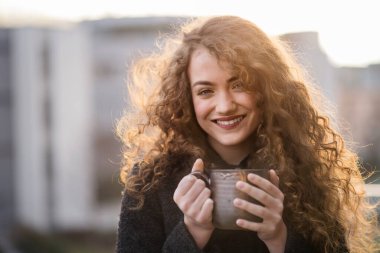 Kıvırcık saçlı güzel bir kadın için sabah rutini. Oturma odasında yerde oturuyor, bir fincan kahve içiyor ve kameraya bakıyor. Pencereden..