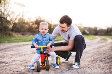 Çocuk bisiklete binmeyi öğreniyor, baba ona yardım ediyor. Babalar Günü.