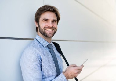Yakışıklı iş adamı akıllı telefondan kayıyor. Ofis binasının önünde duruyor ve işe gidiyor. Müdür gülümsüyor, şehir ortamında açık havada..