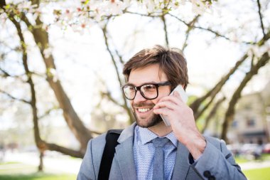 Şehir sokağında duran akıllı telefondan yakışıklı bir iş adamı arıyor. Uzaktan çalışıyor, iş toplantısını bekliyor. Müdür gülümsüyor, şehir ortamında açık havada..