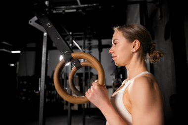 Spor salonundaki halkaların yanında duran güzel bayan egzersiz ve yüzüklere hazırlanıyor. Fiziksel ve zihinsel sağlık için rutin çalışma.