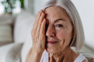 Gri saçlı, yumuşak gülüşlü, kameraya bakan güzel olgun bir kadının portresi. Yüzün önünde el ele.