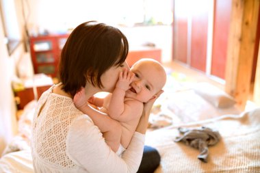 Anne yatağa uzanmış küçük bebekle oynuyor. Koşulsuz baba sevgisi, Anneler Günü.
