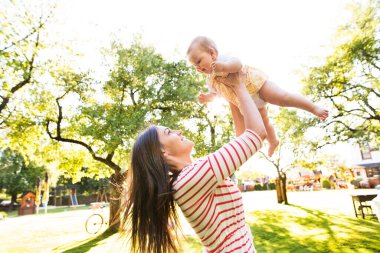 Anne, bebeği elinde tutuyor, onunla oynuyor, eğleniyor. Düşük açılı çekim.