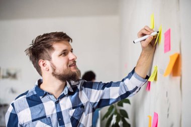 Adam renkli yapışkan notlar üzerine fikirler yazıyor. Girişimci bir şirkette yeni bir proje üzerinde çalışan meslektaşlar. Eş zamanlı çalışma alanında çalışmak