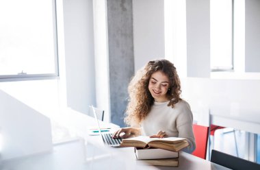 Kütüphanedeki genç bayan öğrenci, son projeye odaklanıyor, sunum. Üniversite öğrencisi final sınavına hazırlanıyor, yazıyor.