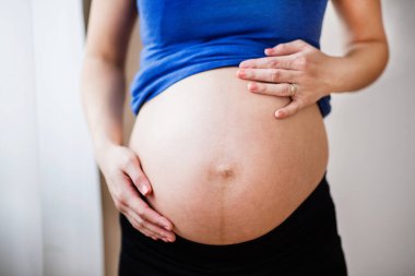 Tanımlanamayan hamile bir kadın çıplak karnına dokunuyor. Hamilelik sırasında sağlık sigortası..