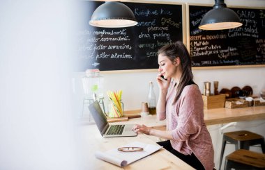 Güzel bir kadın küçük bir lokantada telefon görüşmesi yapıyor. Kadın işyeri sahibi. Yan görünüm.