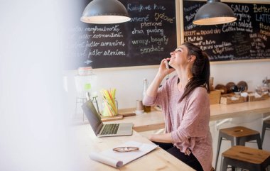 Güzel bir kadın küçük bir lokantada telefon görüşmesi yapıyor. Kadın işyeri sahibi. Yan görünüm.