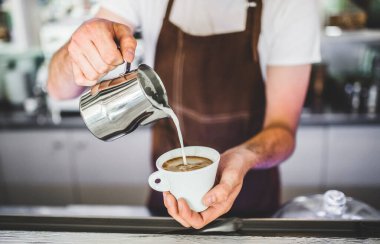 Barista kahvecide çalışıyor, latte hazırlıyor, cappuccino yapıyor. Önlüklü barmen kahve hazırlıyor.