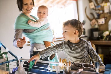 Küçük oğlu annesine ev işlerinde yardım ediyor, çamaşırları kurutma sehpasına asıyor. Haftalık ev işleri, aile için hafta sonu aktiviteleri.